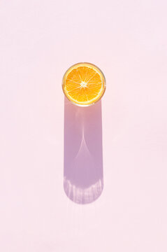 Glass of drink with orange on a pink background. Aesthetic long shadow glass summer concept.