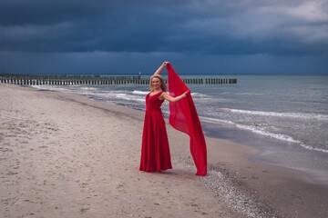Interesting holiday seaside concept. Beautiful woman in a red dress on the seashore.