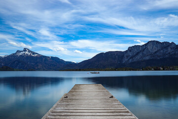Beautiful landscape view of a wooden pier on the lake against mountains and blue cloudy sky - Powered by Adobe