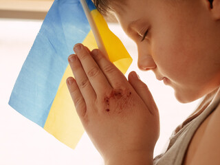 Boy praying for peace in Ukraine holding a national flag with wounded hands