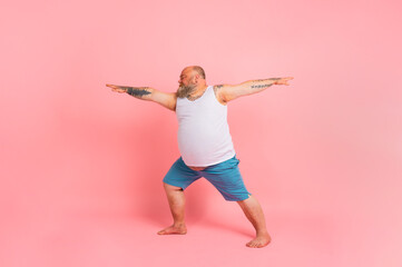 Funny man with beard in yoga position on studio pink background