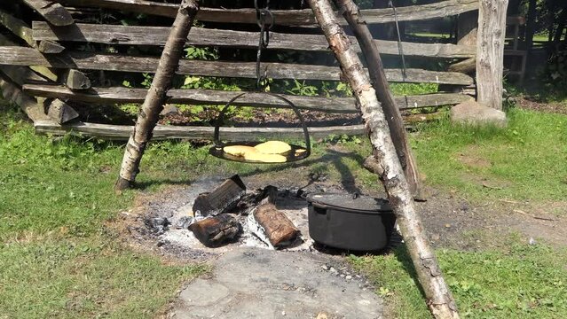 Old woman cooking bread on a griddle over a fire outdoors at The Ulster America Folk Park in Northern Ireland