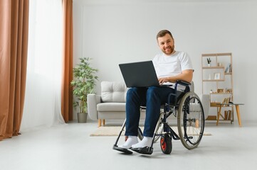 Work at home. Paralyzed male person holding laptop on knees and keeping smile on face while looking at screen