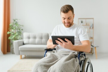 Man in wheelchair using tablet computer at home. Positive retired male with physical disability...