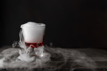 vasito de coctel con reacción química de hielo seco, fondo negro y base de piedra