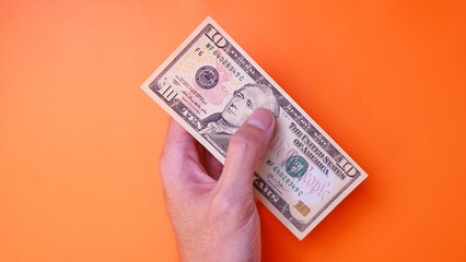 Man's hand is making a payment. Business Investment Economy Saving Loan Income Money and Finance concept. Male hand showing dollar cash on an orange background. Ten Dollar 10 USD. Prosperity concept.