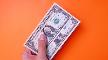 Man's hand is making a payment. Business Investment Economy Saving Loan Income Money and Finance concept. Male hand showing dollar cash on an orange background. One Dollar 1 USD. Prosperity concept.