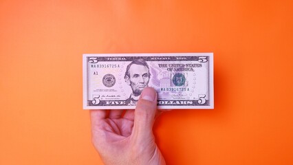 Man's hand is making a payment. Business Investment Economy Saving Loan Income Money and Finance concept. Male hand showing dollar cash on an orange background. Five Dollar 5 USD. Prosperity concept.