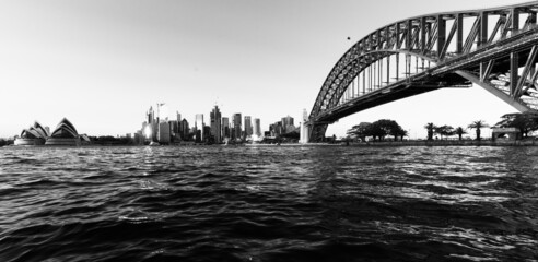 Black and white shot of the Sydney Harbour Bridge with the cityscape against a cloudless sky