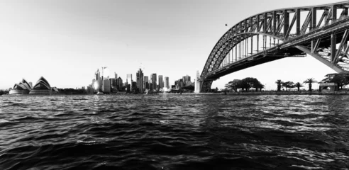Fotobehang Sydney Harbour Bridge Zwart-wit opname van de Sydney Harbour Bridge met het stadsbeeld tegen een wolkenloze hemel