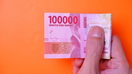 Indonesian Rupiah the official currency of Indonesia. Man's hand is making a payment. Male hand showing Indonesian Rupiah note. Business Investment Economy Loan and Finance concept Uang 100.000 Rupiah