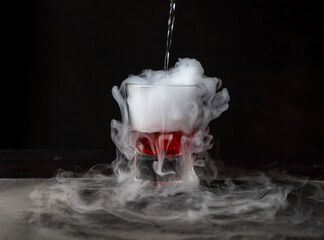 Bebida roja con hielo seco sobre fondo negro y con base de piedra. reacción química con Humo...