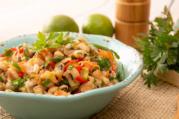 Bean salad, an homemade salad with beans, tomatoes, onions, peppers and herbs close-up on a plate on a table. Horizontal top view from above.