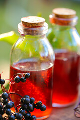 Elderberry syrup.Sambucus syrup in a glass bottle on a wooden table in the summer garden in the sun.Green pharmacy and homeopathy.Sweet healthy elderberry syrup. 