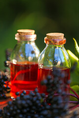 Elderberry syrup in a bottle and bunches of elderberries on a wooden table in the summer garden in the sun.Green pharmacy and homeopathy.Sweet healthy elderberry syrup. 