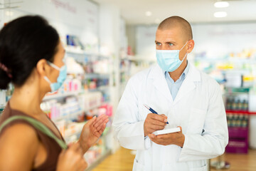 Pharmacist in protective mask writes in notebook the name of the drugs that the buyer tells him to
