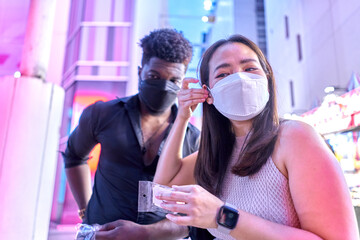 Asian woman with mask trying on earrings with a friend in a street market
