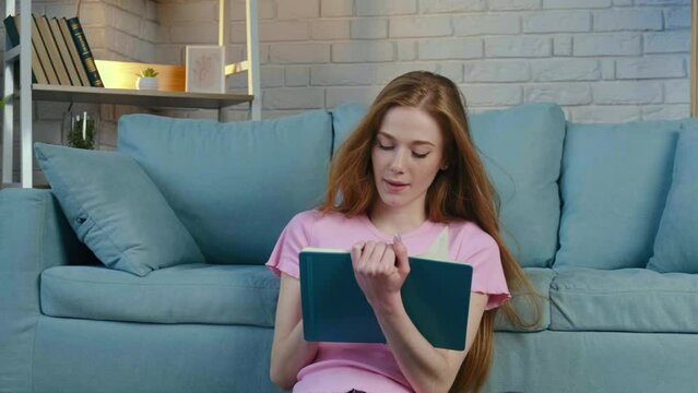 Portrait of a dreamy woman with red hair sitting on floor writing something, creating poem. Close-up view. Beautiful young girl.