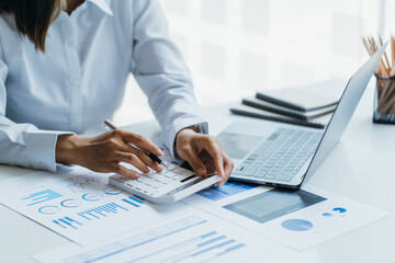 Asian woman is pointing at the report graph and has laptop on the front. Maybe preparing data for marketing report. window light