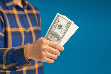 Hand holding of a US dollars banknote while standing on a blue background