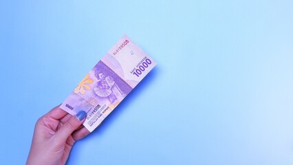 Indonesian Rupiah the official currency of Indonesia. woman's hand is making a payment. Female hand showing Indonesian Rupiah note. Business Investment Economy and Finance concept. Uang 10000 Rupiah.