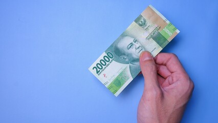 Indonesian Rupiah the official currency of Indonesia. Man's hand is making a payment. Male hand showing Indonesian Rupiah note. Business Investment Economy and Finance concept. Uang 20000 Rupiah.