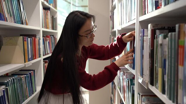 Japanese student girl look through books in library or bookstore picking novel or material for course work in university. Concentrated young asian woman tutor teacher search for textbook for lecture