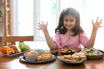 Cute little Indian girl is enjoying her favorite Indian food, surprised girl raised hands