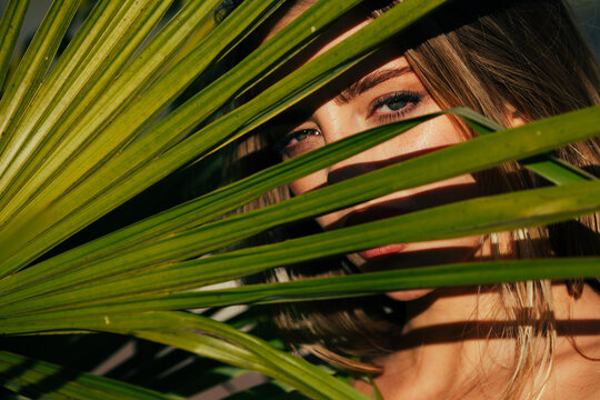 Closeup portrait of beautiful woman with shadows of palm leaf on her face. Natural beauty on tropical leaf background. Young girl with healthy skin of face and palm leaves. Summer spa and wellness.