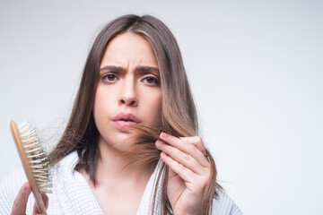 Hair loss. Woman is upset of hair loss. Portrait of sad girl with problem hair, isolated. Worried girl holding long damaged unhealthy hair in hand.