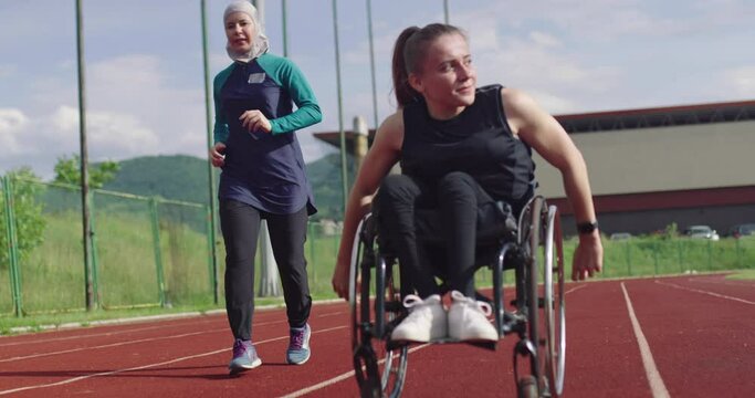 A female person with disabilities riding a wheelchair on a athletics training track with muslim woman wearing hijab sportwear