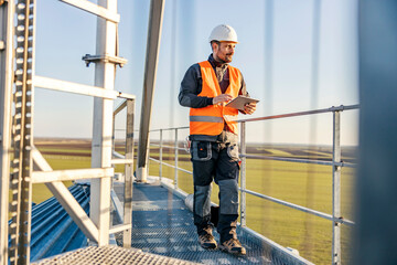 An industry worker standing on height and using tablet for silo supply purposes.