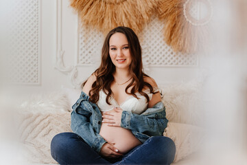 pregnant woman in denim jacket with naked tummy sitting in bed