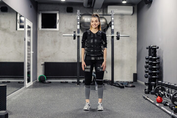 Fototapeta na wymiar Sportswoman in a special EMS suit standing in the middle of the gym. 