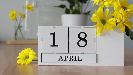 Spring month April 18. A woman's hand turns over a cubic calendar. White perpetual calendar on the table next to yellow flowers. Change the date in a month. day in the month. memorial day, amateur rad