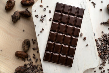 Dark bitter chocolate bar with cocoa beans on a wooden white background, top view. delicious chocolate. Space for text