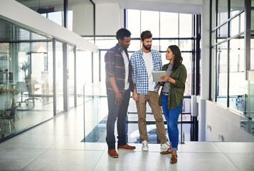 Making innovative ideas happen. Shot of three young designers working on a digital tablet in a modern office.