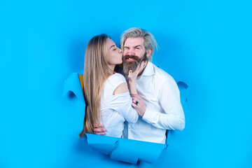 Couple through hole in blue paper, copy space for text or slogan. Discount and sale, people hole background. Surprised couple of bearded man and happy woman making hole in paper looking through hole.