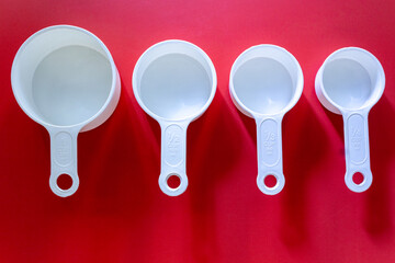 Set of white measuring cups, measuring spoons use in cooking lay on wooden red background in top view