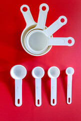 Set of white measuring cups, measuring spoons use in cooking lay on wooden red background in top...