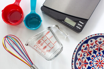 Measuring cups made from colorful plastic and glass, digital scale and whisk use in cooking lay on...