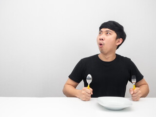 Man holding cutlery sit at the table feeling excited and looking at copy space