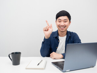 Man smiling and point finger at copy space at workplace and laptop on the desk