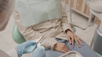 Tilt slowmo of young Muslim woman in headscarf having dental appointment at modern clinic, sitting at dental chair and listening to stomatologist