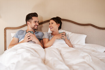 Fototapeta premium Starting off our morning on a warm note. Shot of a happy young couple drinking coffee in bed in their bedroom at home.