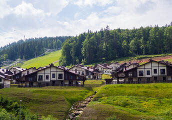 Plakat Scenic summer view of winter mountain ski resort with house cottages with forest and skiing slope in Bukovel, Ukraine. 