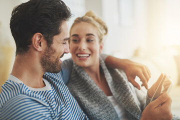 Fototapeta premium Sharing the things they love with the convenience of technology. Shot of a young couple using a digital tablet on their sofa at home.