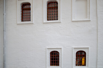 Fototapeta na wymiar White wall of house with red bars on windows