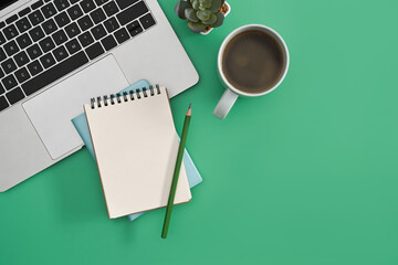 Stylish workplace with laptop computer, notepad and coffee cup on green background.