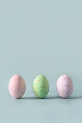 Three colorful pastel eggs stand on blue background. Happy Easter vertical greeting card with copy space.